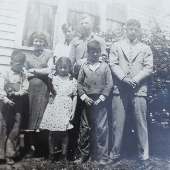Family poses in front of a house. Two adults and five children. Black and white photo.