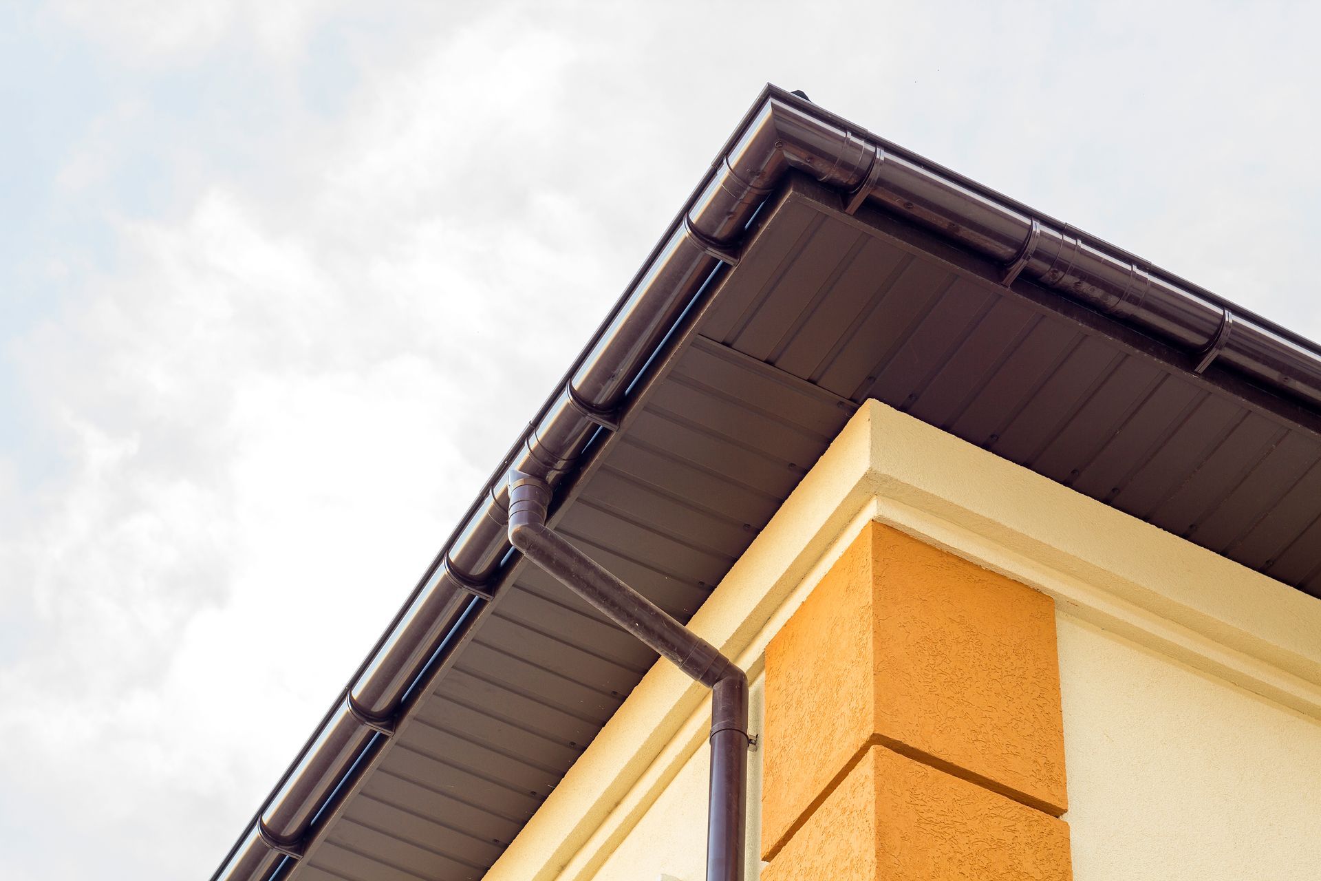 Brown roof corner with gutter and downspout on a beige and orange wall.
