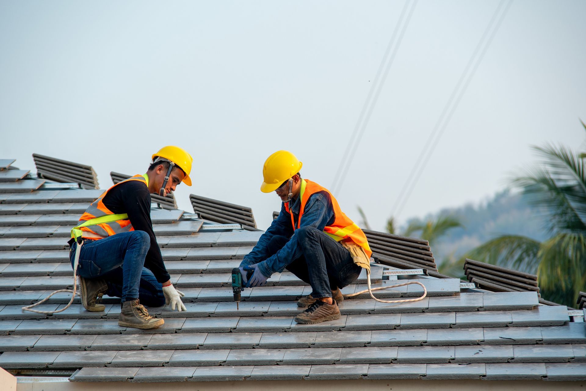 Two construction workers installing roof tiles, wearing hard hats and safety vests. Two construction workers installing roof tiles, wearing hard hats and safety vests.