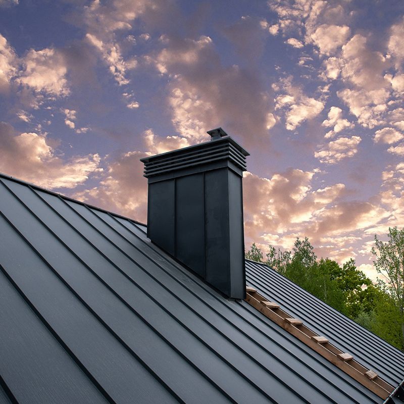 Black metal roof with chimney against a cloudy sky. Black metal roof with chimney against a cloudy sky.