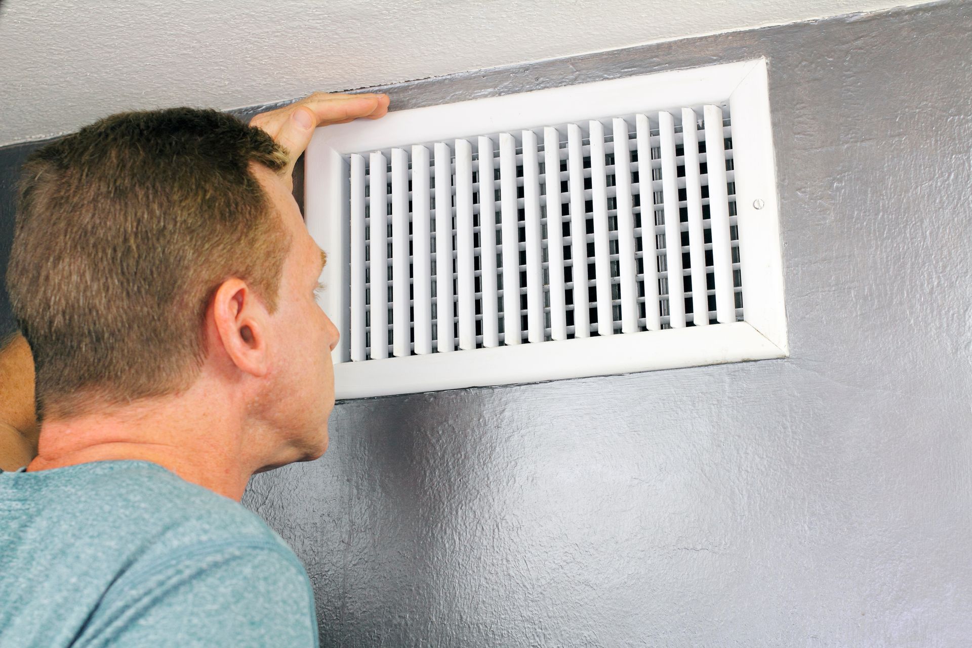 Man inspecting an air duct vent on a wall. Man inspecting an air duct vent on a wall.