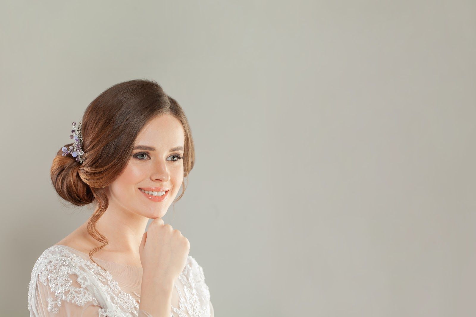 Smiling woman in a white lace dress with an elegant updo against a plain gray background