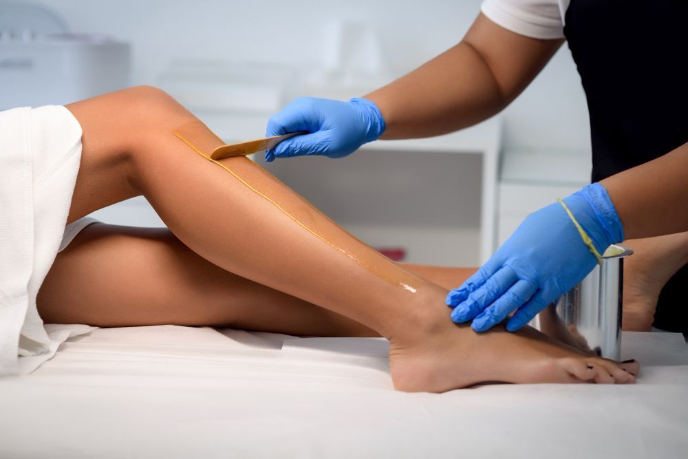 Waxing a client's leg with blue-gloved hands in a spa treatment room