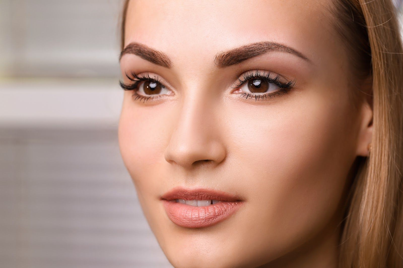 Close-up portrait of a woman with makeup and light brown hair, looking slightly to the side against a soft background