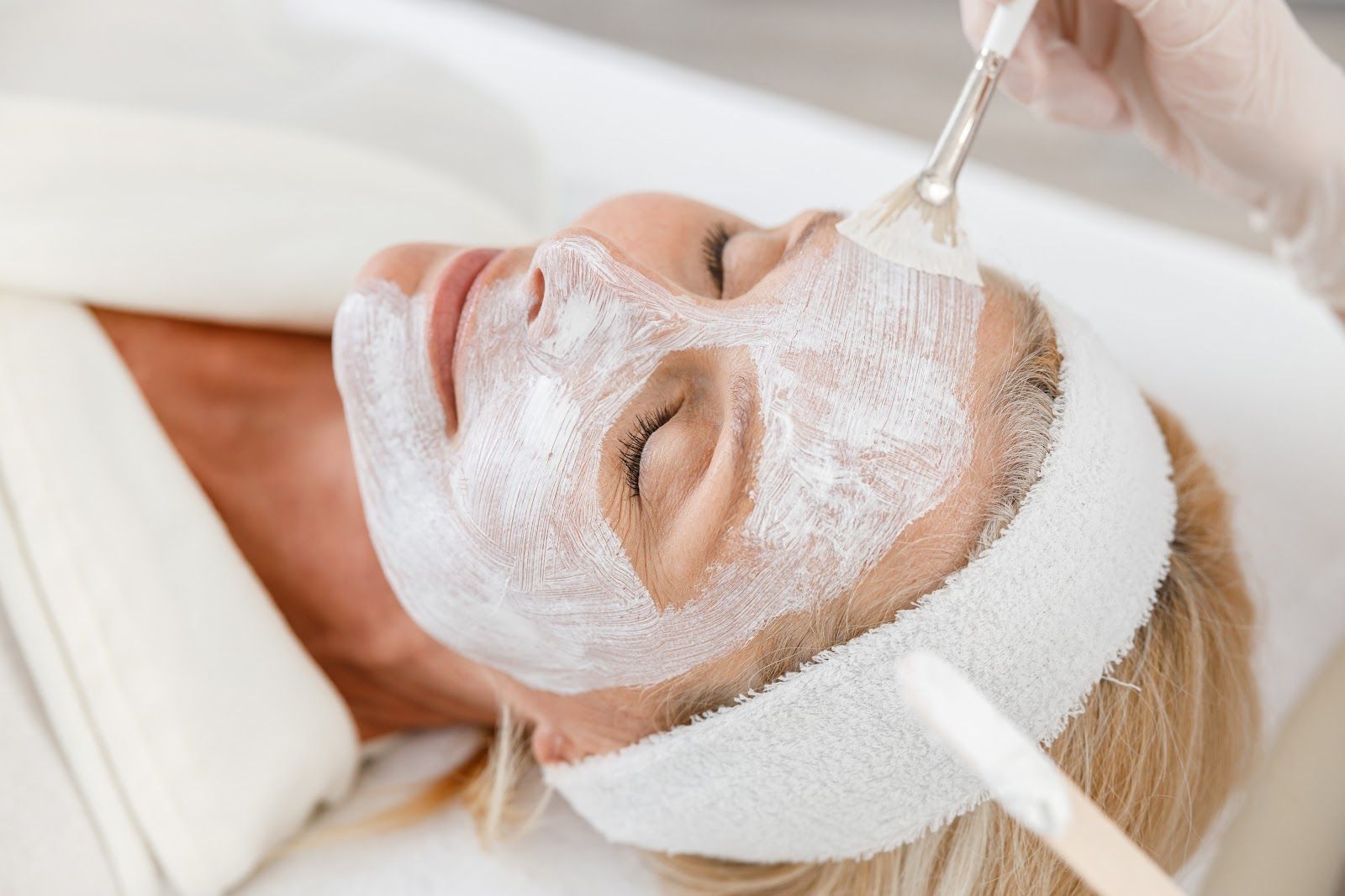 Person receiving a facial treatment with white cream applied, lying on a spa bed with a headband