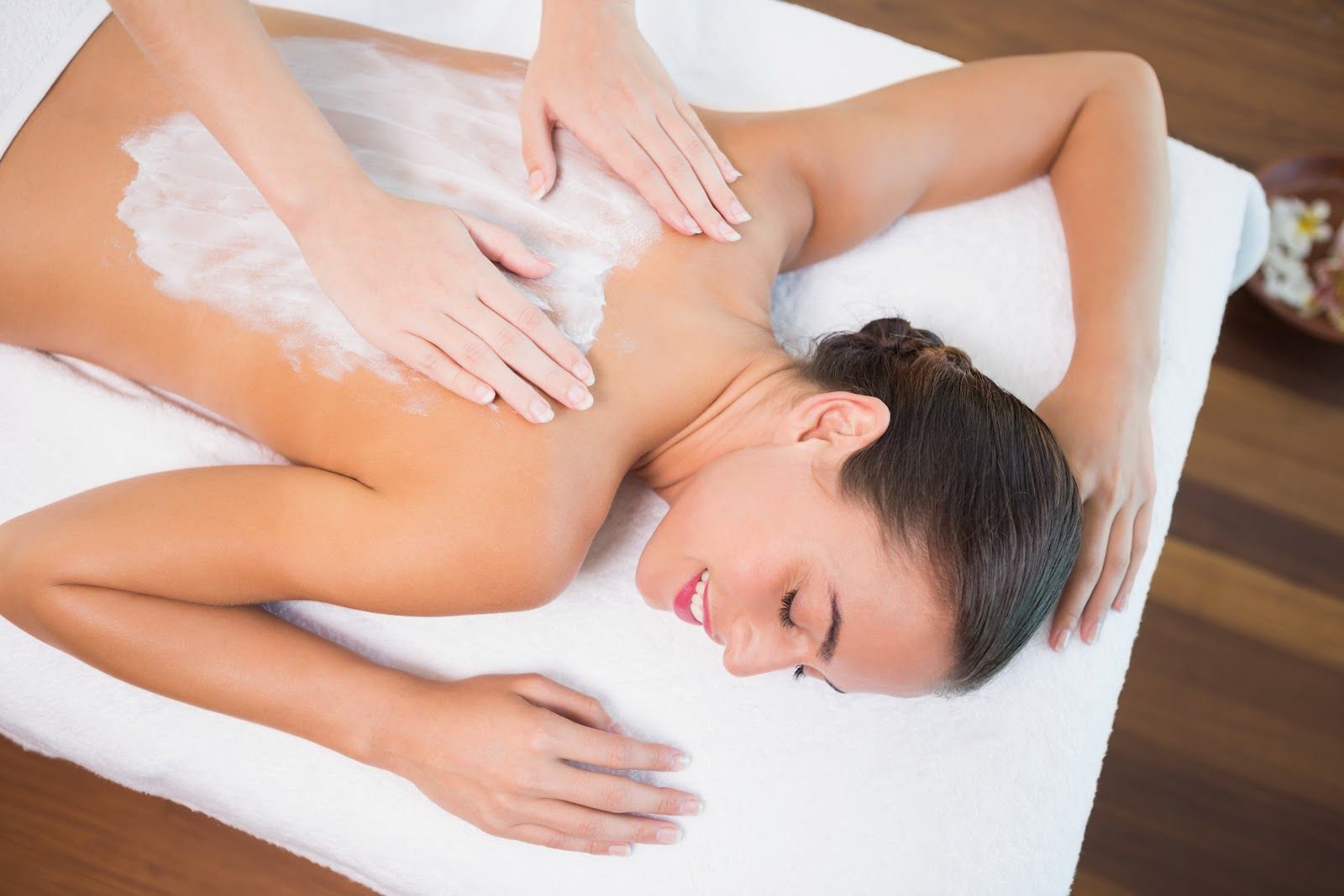 Spa massage on a woman lying face down on a treatment table, with hands applying lotion on her back