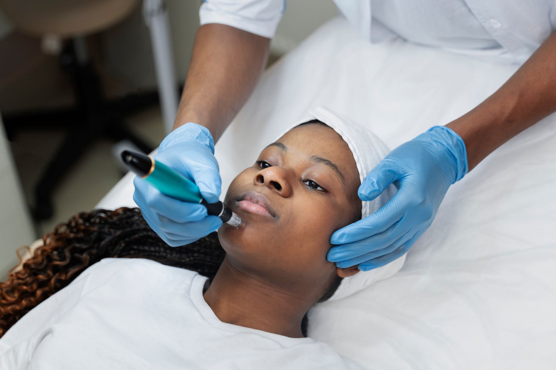 Esthetician applying a facial treatment to a client lying on a treatment bed, using blue gloves