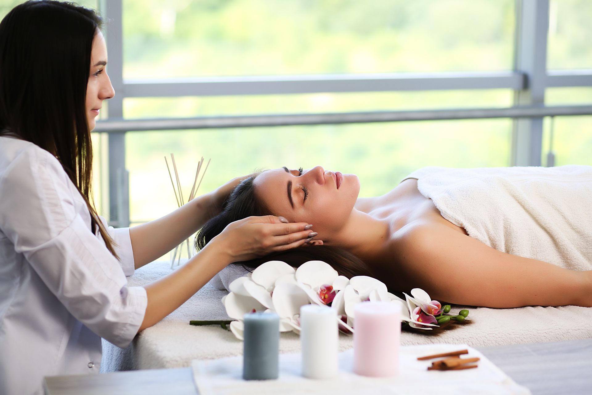Massage therapist giving a head massage to a reclining client in a bright spa room