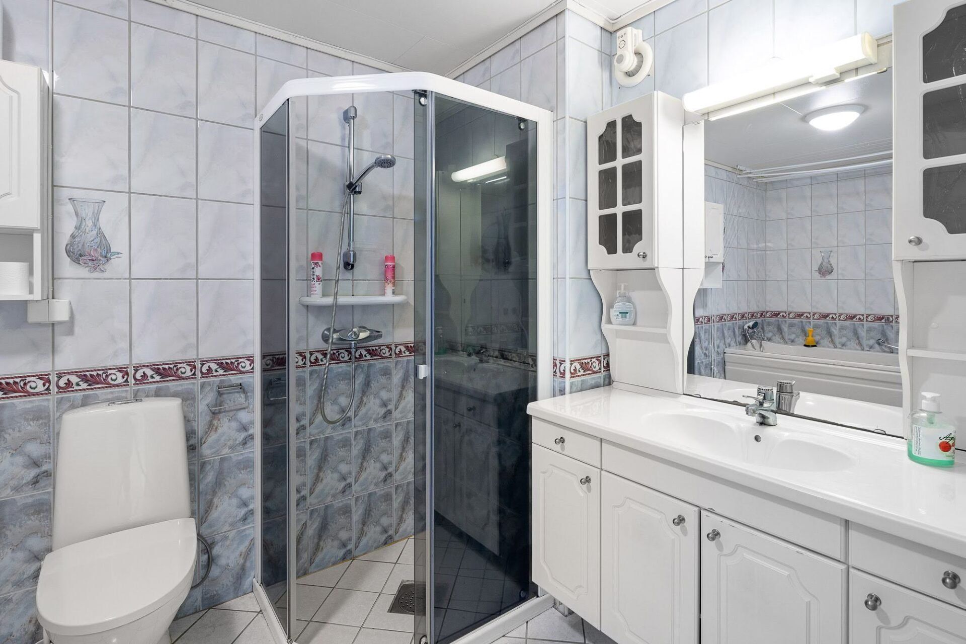 Bright tiled bathroom with shower, toilet, and white vanity with large mirror.