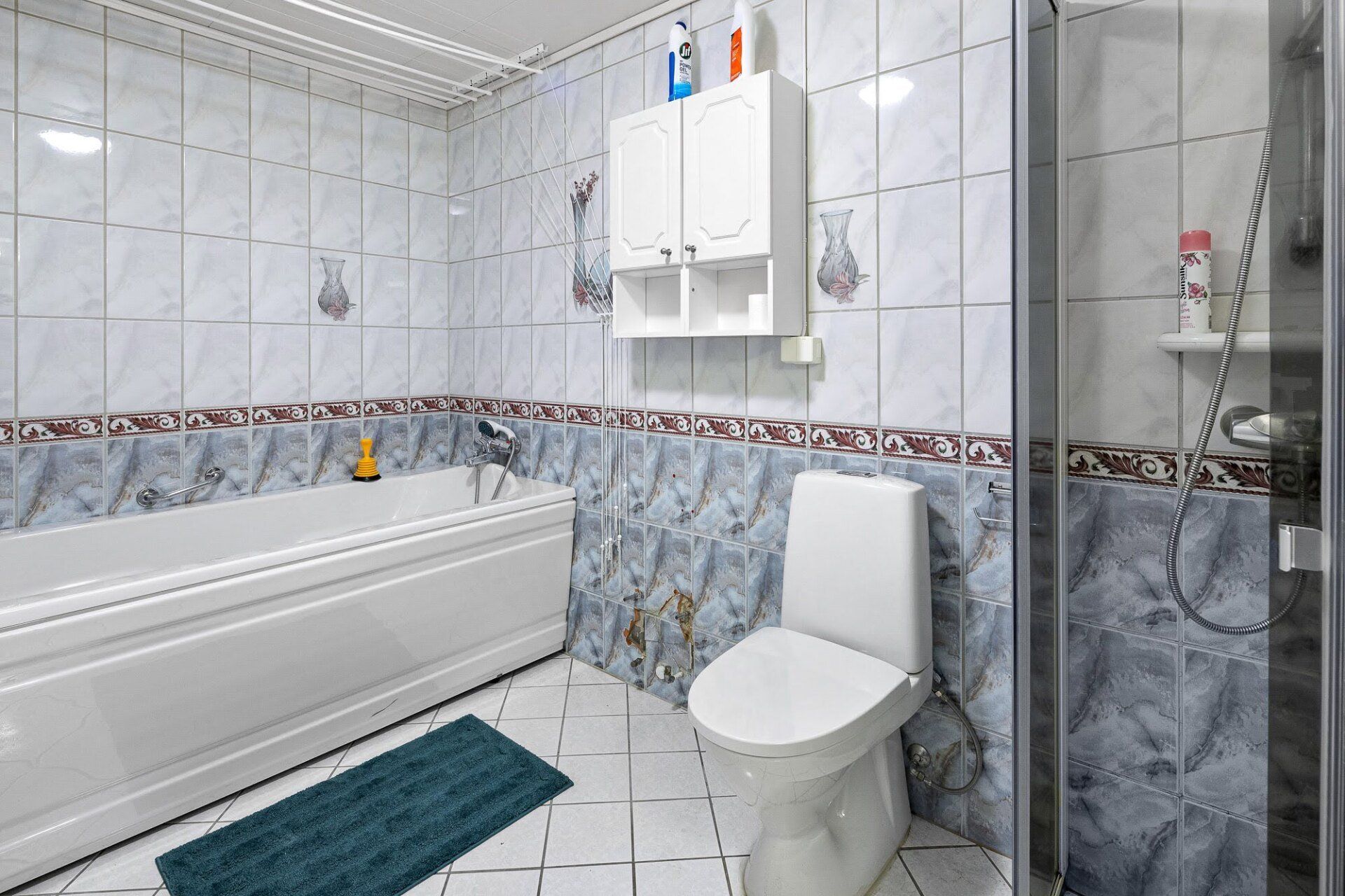 Bright white bathroom with bathtub, toilet, shower, and blue floor mat.