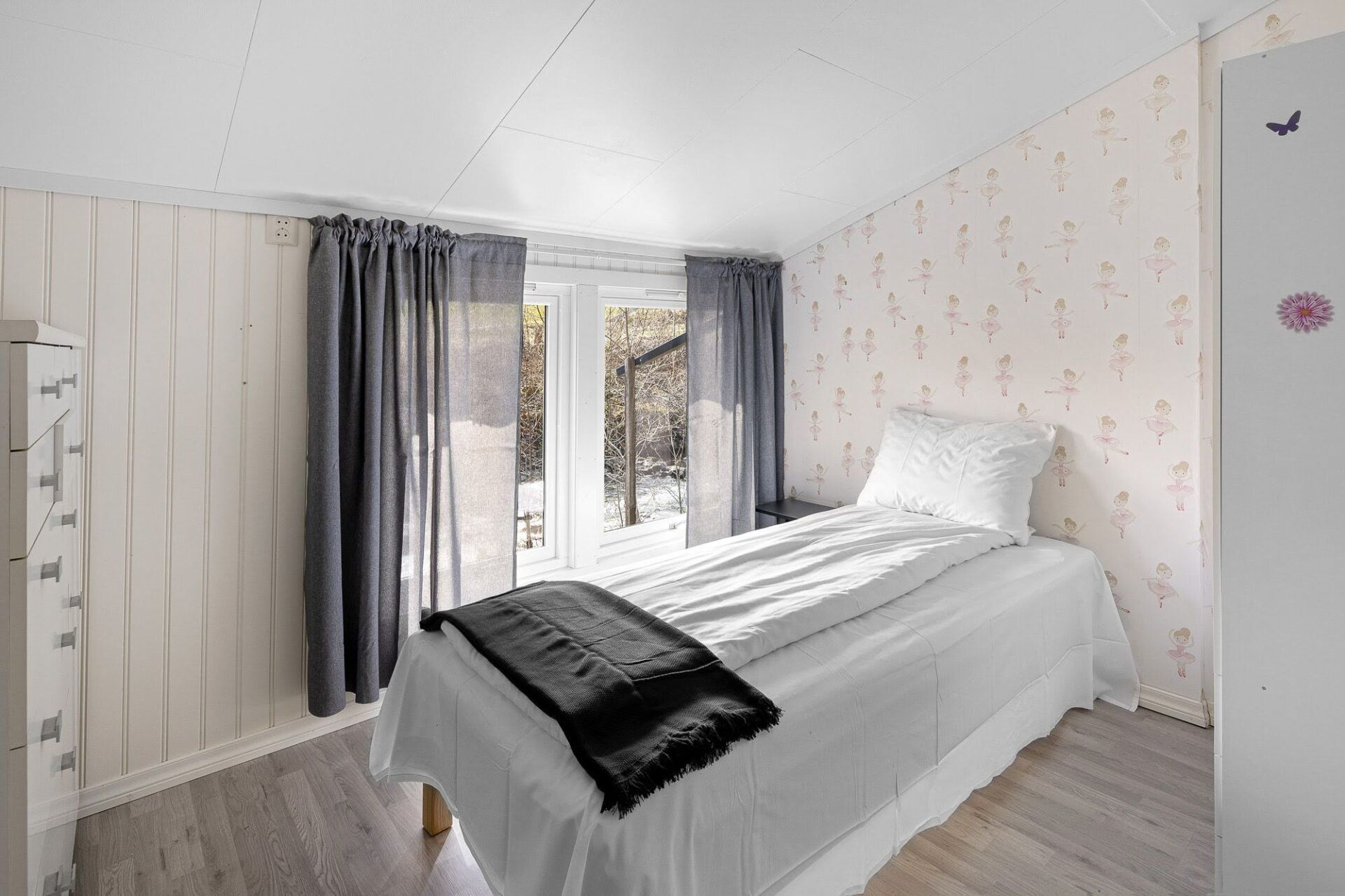 Bright white bedroom with a single bed, gray curtains, and French doors opening to a balcony.