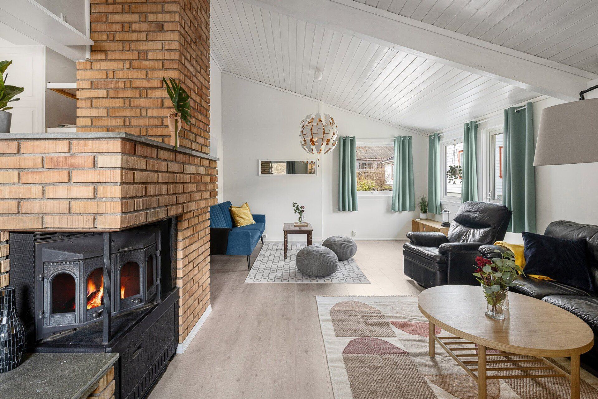 Bright living room with brick fireplace, white vaulted ceiling, black sofa, blue chair, and round coffee table