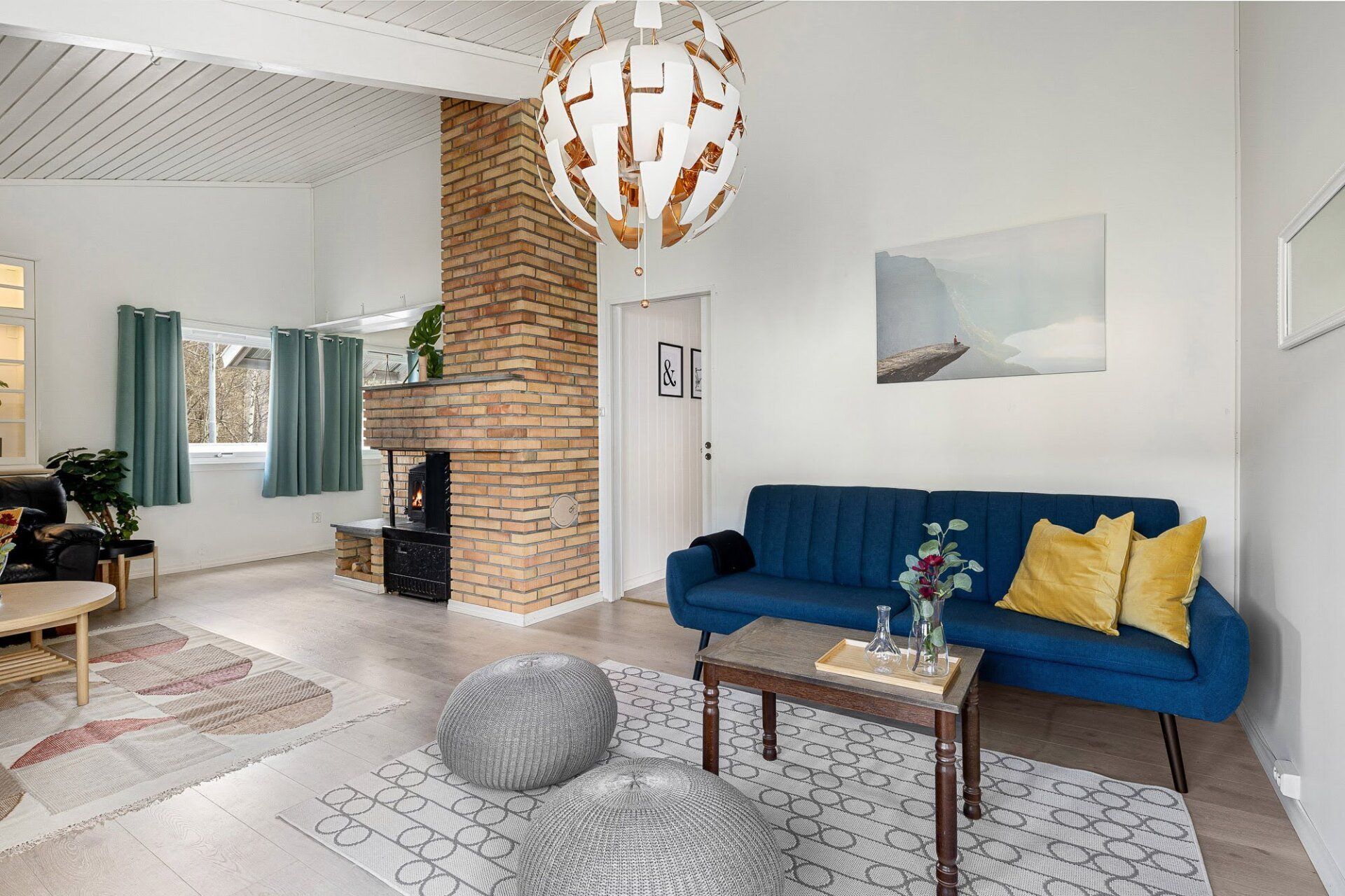 Bright living room with blue sofa, brick fireplace, patterned rug, and hanging pendant light