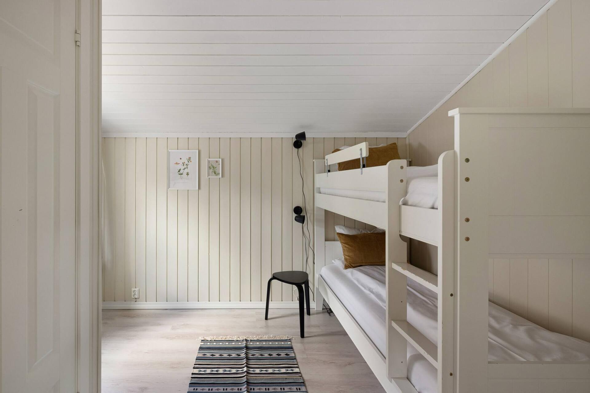 Narrow loft-style bedroom with white walls, bunk beds, stool, and patterned rug.