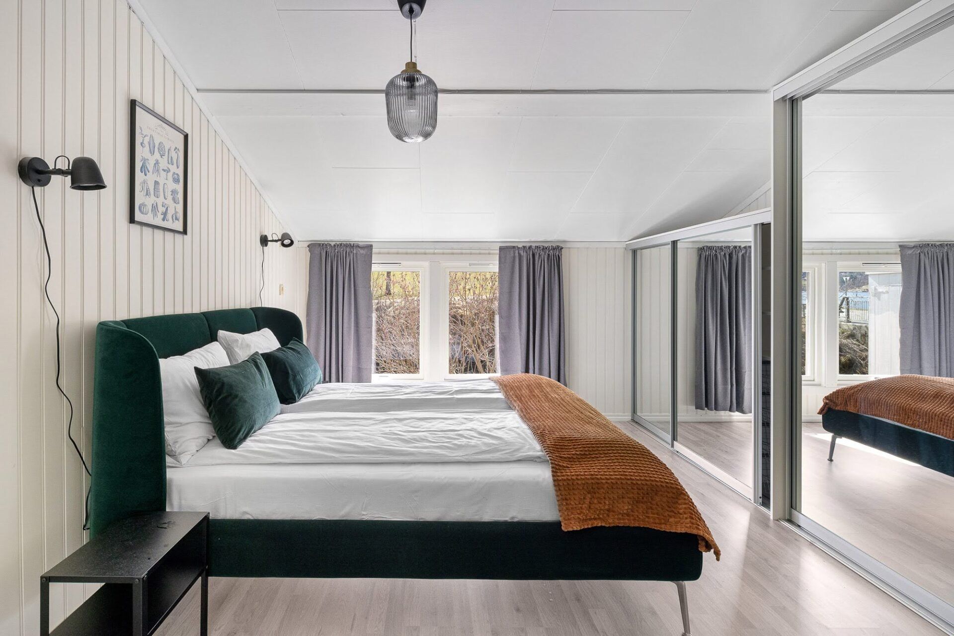 Bright modern bedroom with a green bed, brown throw, large mirror, and curtains by a window