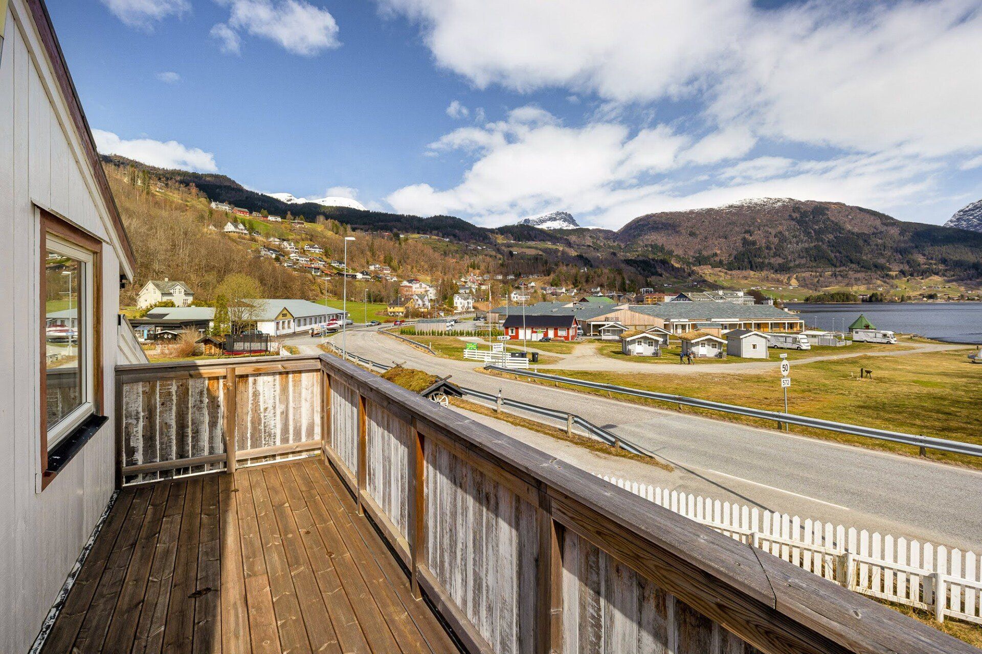 Wooden deck overlooking a lakeside village, hills, and blue water under a cloudy sky
