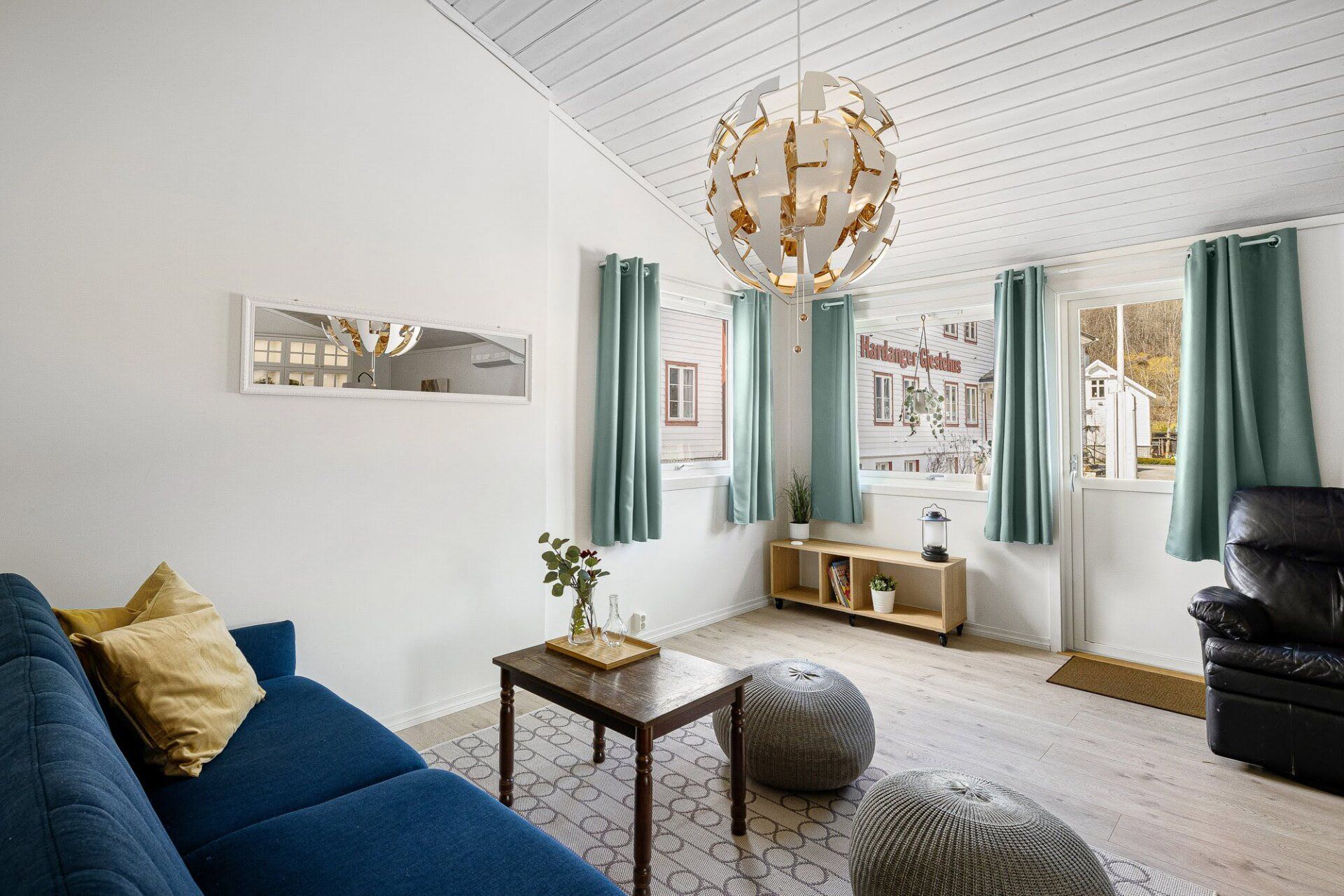 Bright living room with blue sofa, white walls, teal curtains, and a gold chandelier