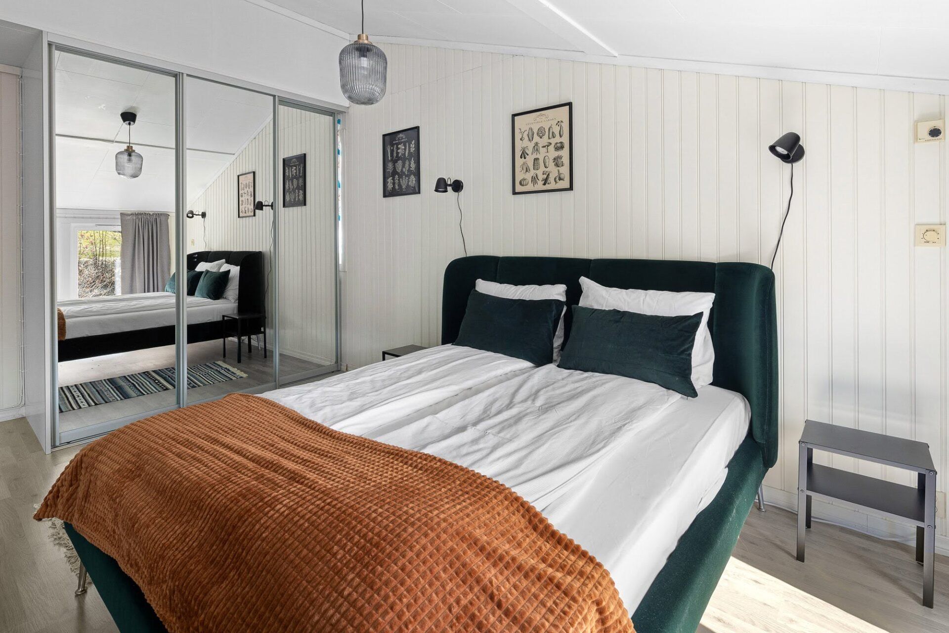 Cozy bedroom with dark green bed, white walls, mirrored closet, and orange throw blanket