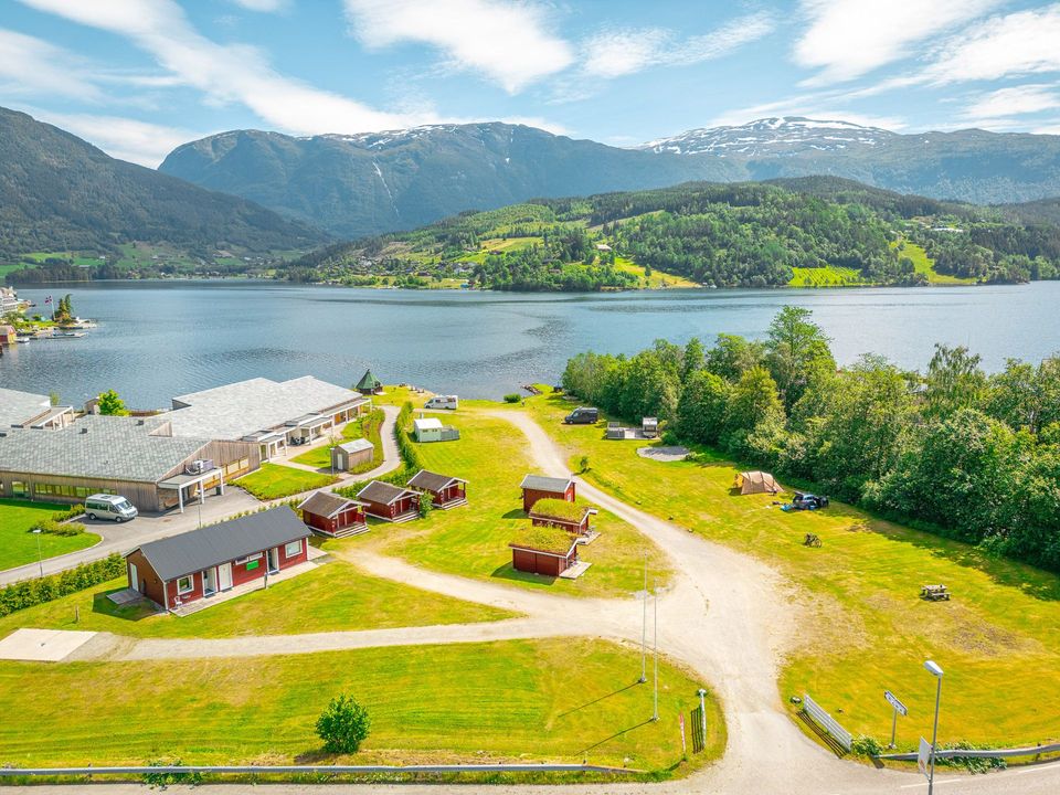 Lakeside campsite with cabins, grassy paths, and mountains under a blue sky