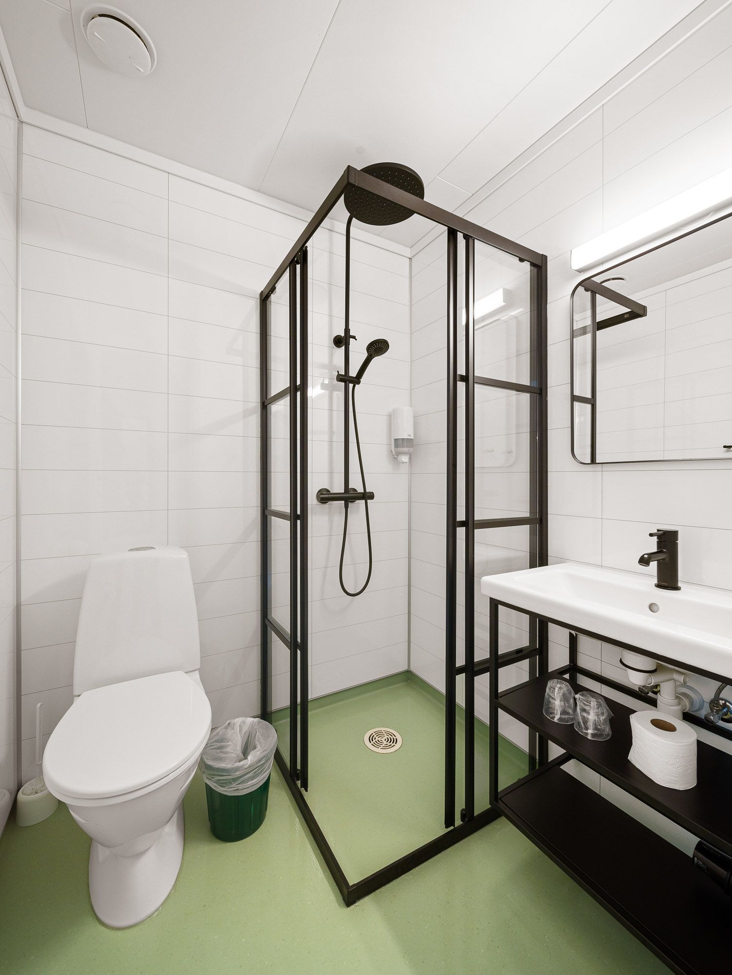 Compact bathroom with toilet, glass shower, and sink vanity on white tile walls.