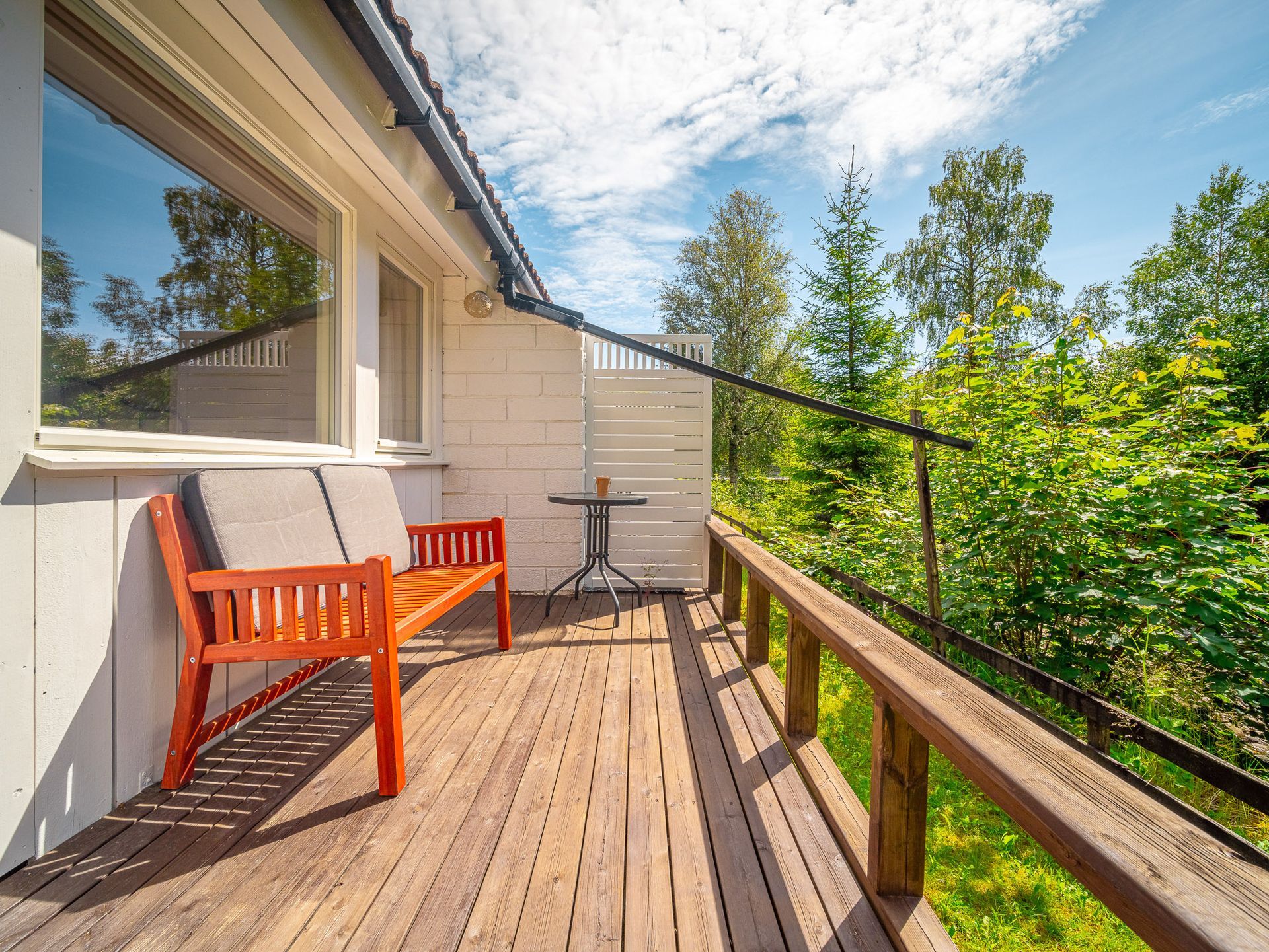 Wooden deck with orange chairs beside a house, overlooking trees and a bright sky