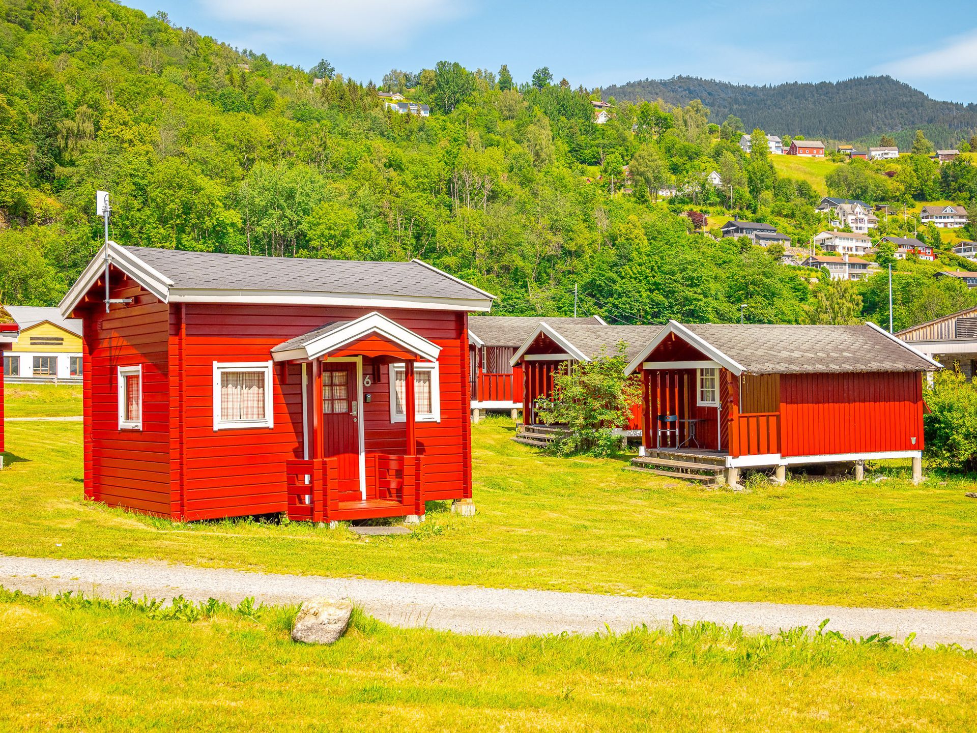 Red cabins on a grassy hillside with green trees and mountains in the background