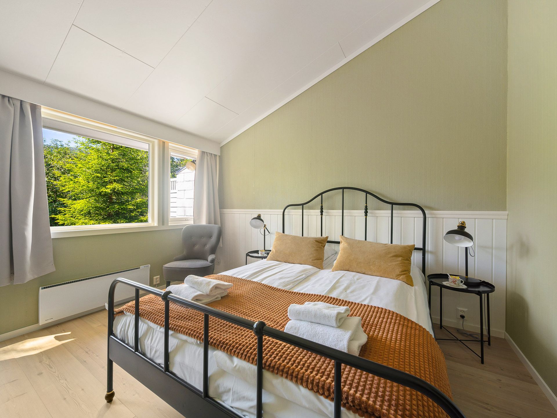 Bright bedroom with black metal bed, orange bedding, and a large window letting in natural light.