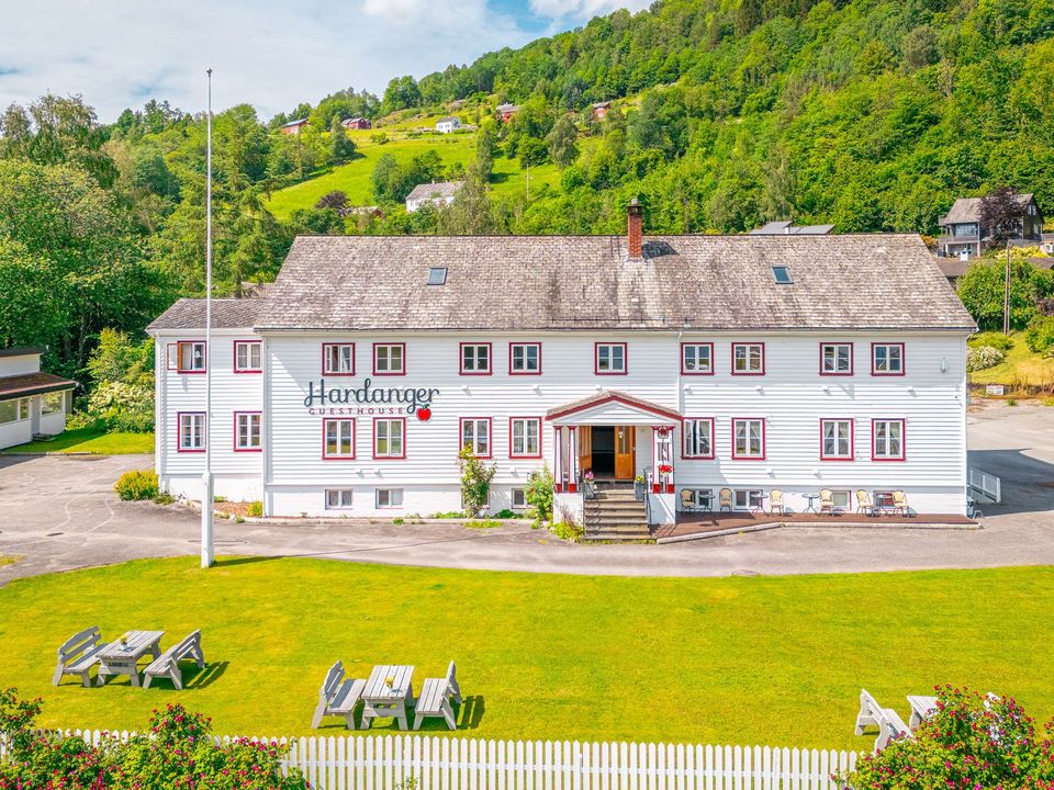 White inn with red trim on a green lawn, set against a wooded hillside.