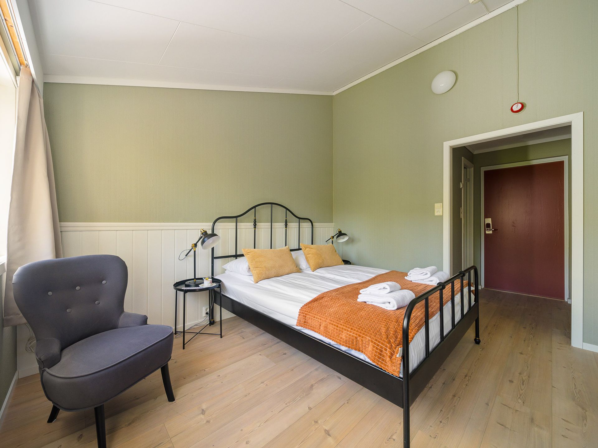 Spartan bedroom with a black metal bed, gray chair, green walls, and a doorway to a hall