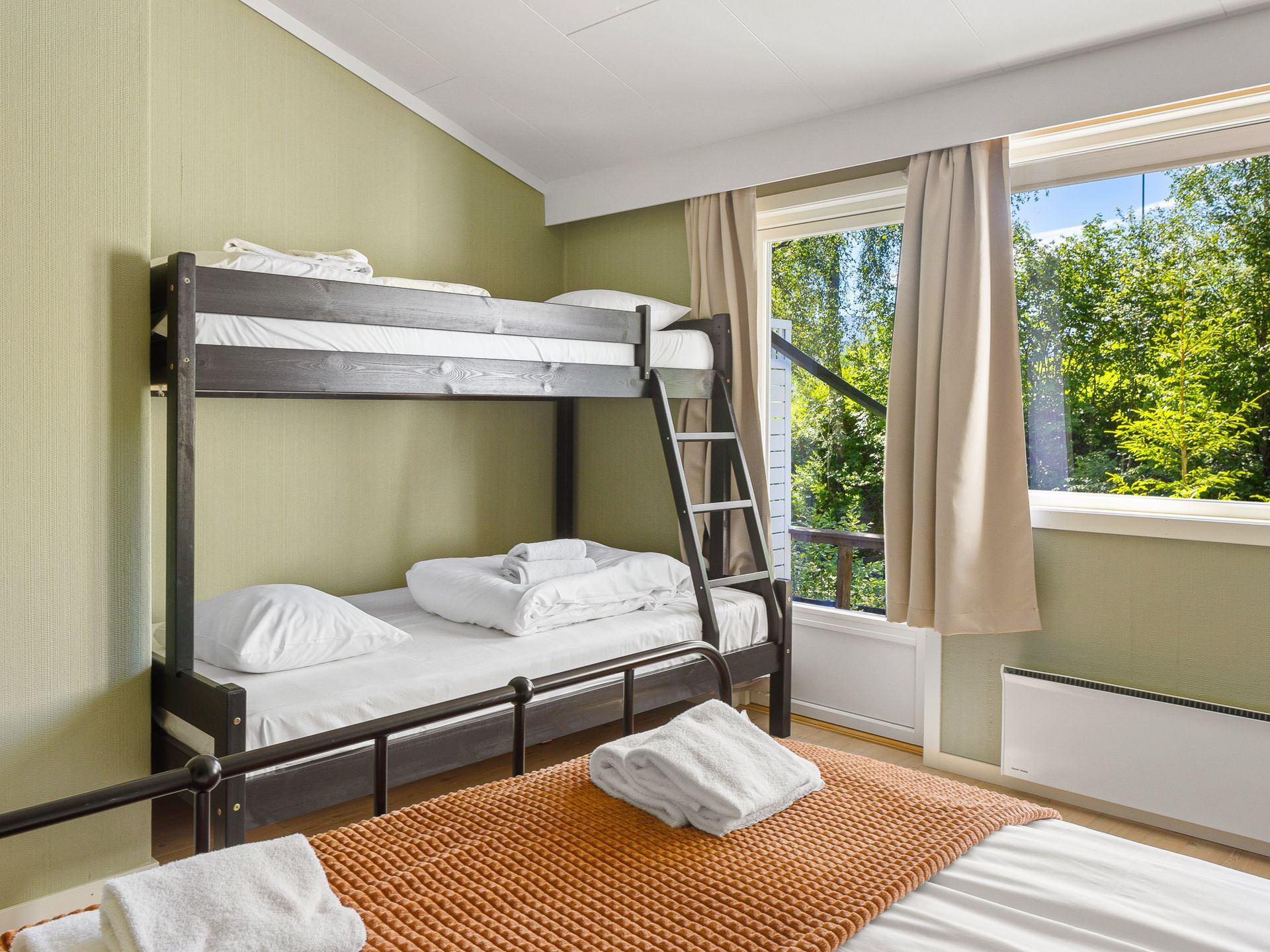 Bright bedroom with dark bunk bed, ladder, large window, and orange blanket on the bed