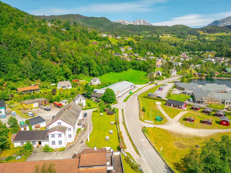 Aerial view of a green hillside village with winding roads, scattered houses, and mountains in the background