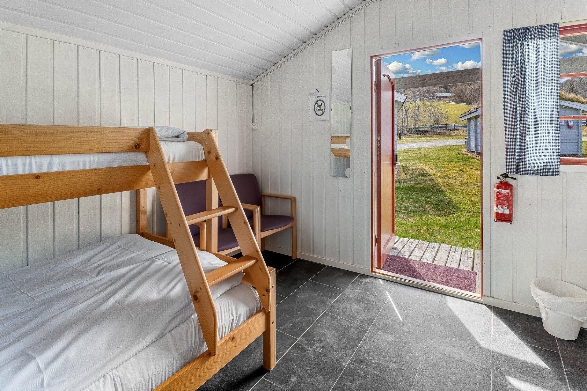 Bunk beds in a white cabin bedroom with an open door to a grassy yard.