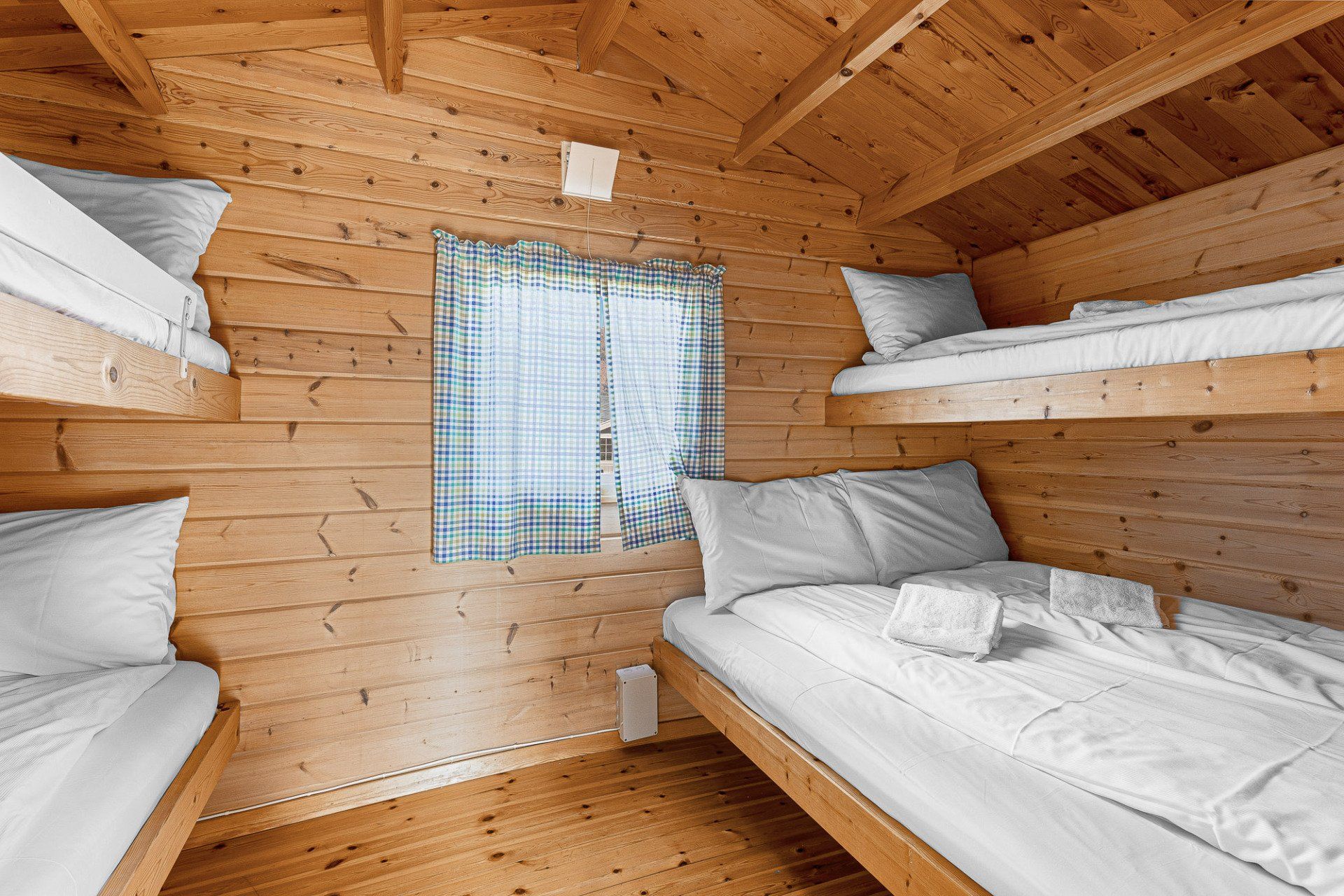 Wooden cabin bunk room with white beds and a small curtained window