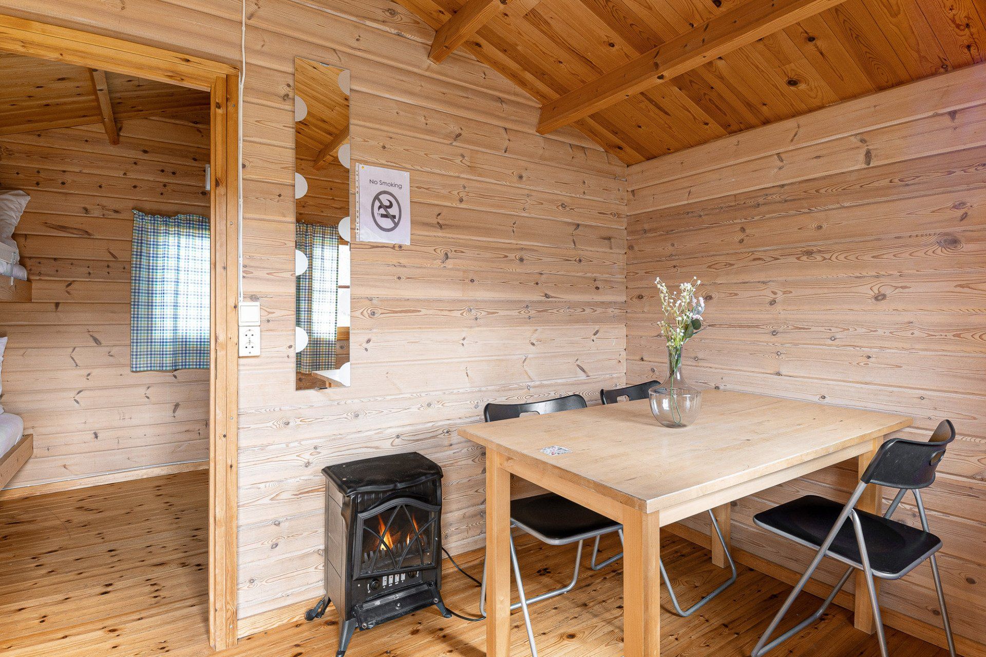 Wood-paneled cabin interior with dining table, chairs, wood stove, and mirror on the wall
