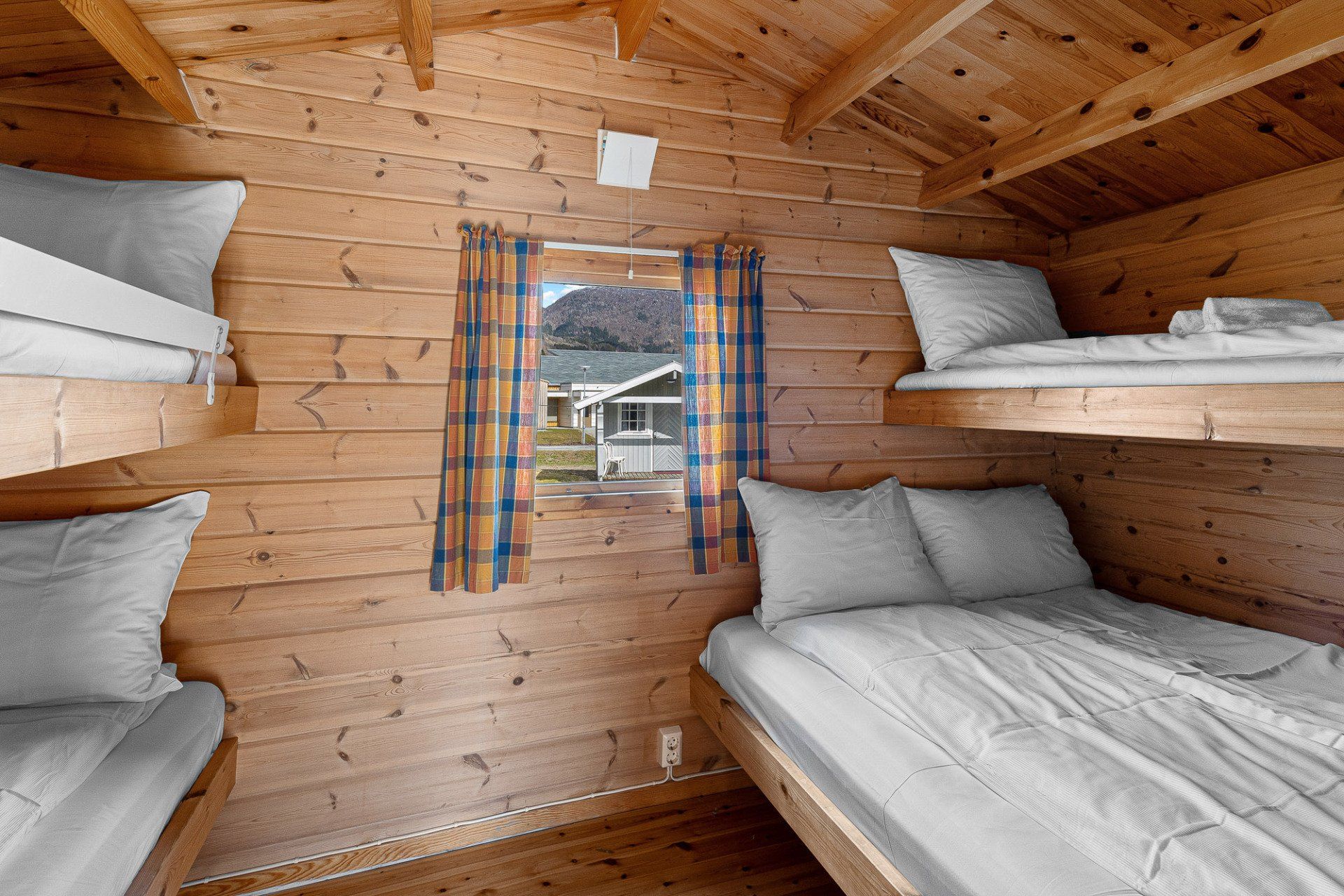 Wood-paneled bunk room with four beds and a small window showing a cabin exterior.