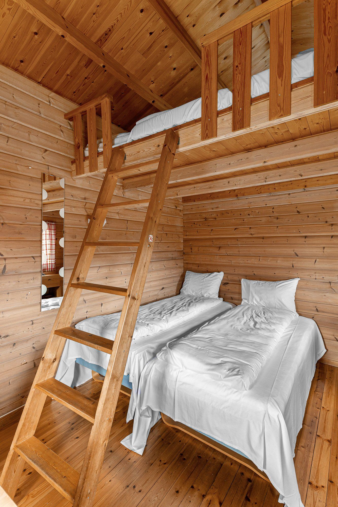 Wooden cabin room with a bunk bed ladder and white bedding under a lofted sleeping area