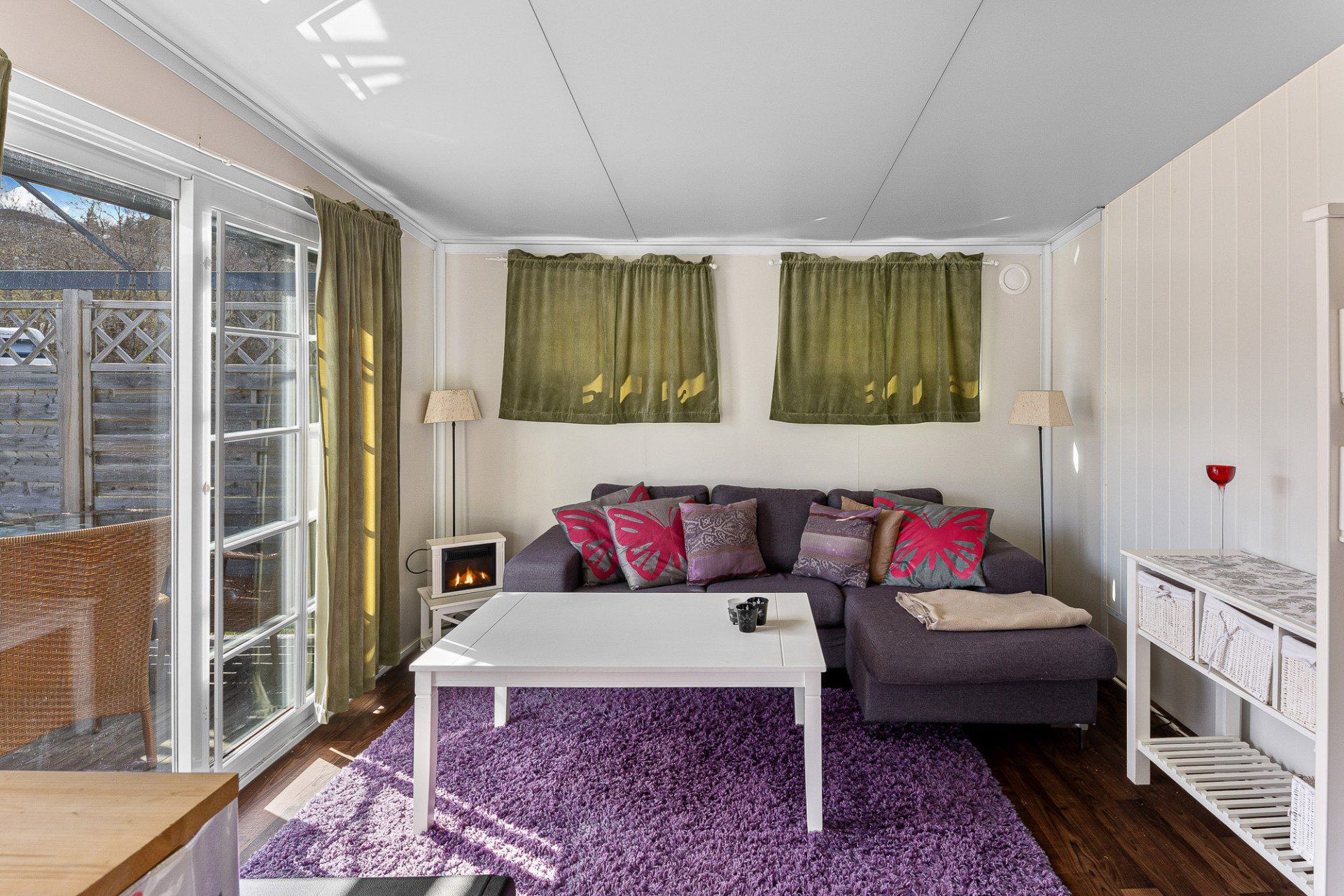 Bright living room with purple rug, gray sofa, white coffee table, and green window valances