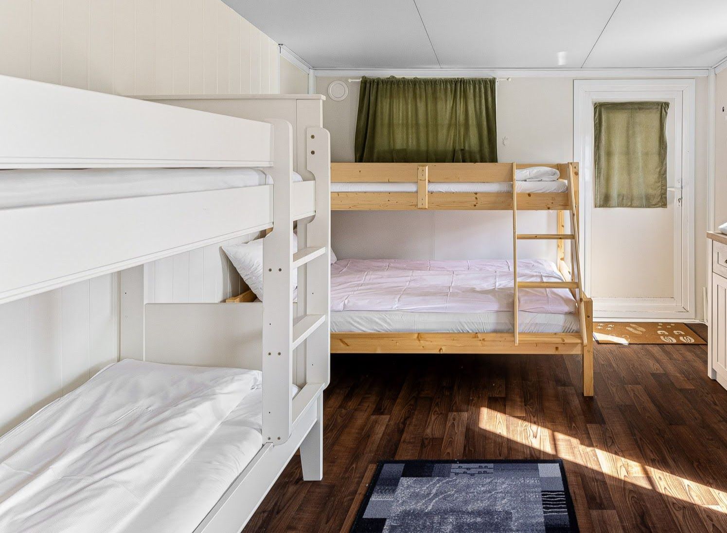 Bright bedroom with white bunk beds, dark wood floor, and a door with a small window.