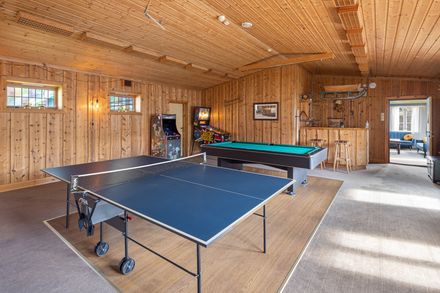 Wood-paneled rec room with a ping-pong table and pool table in warm sunlight