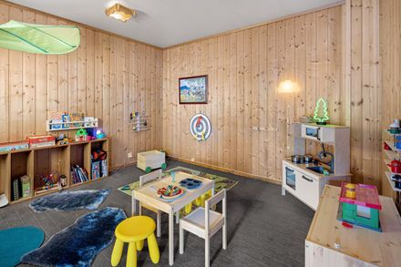 Kids’ playroom with toys, small table, yellow stools, and wood-paneled walls