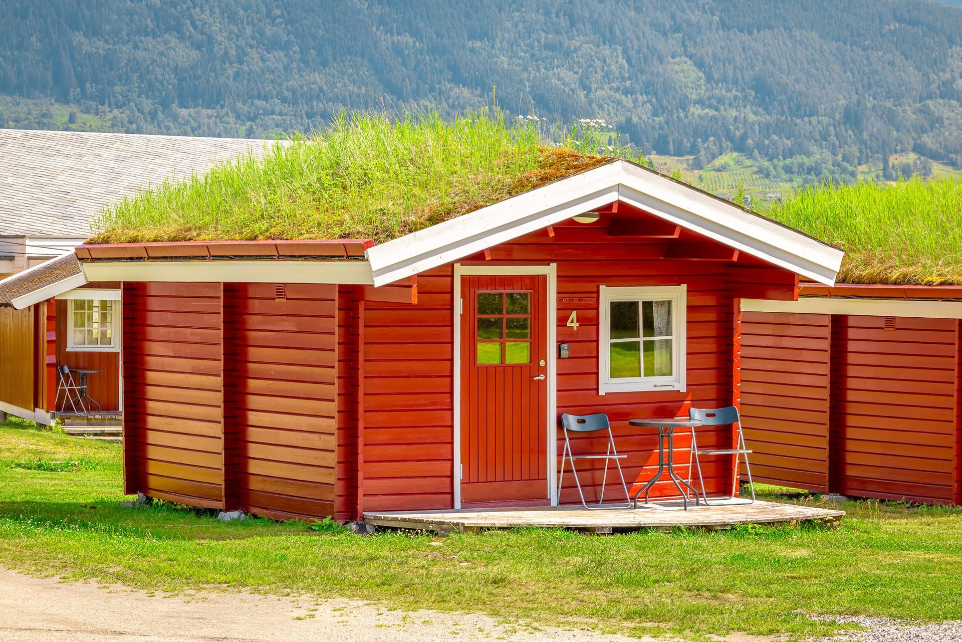 Small red wooden cabin with a green roof and a patio table, set in a grassy mountain landscape