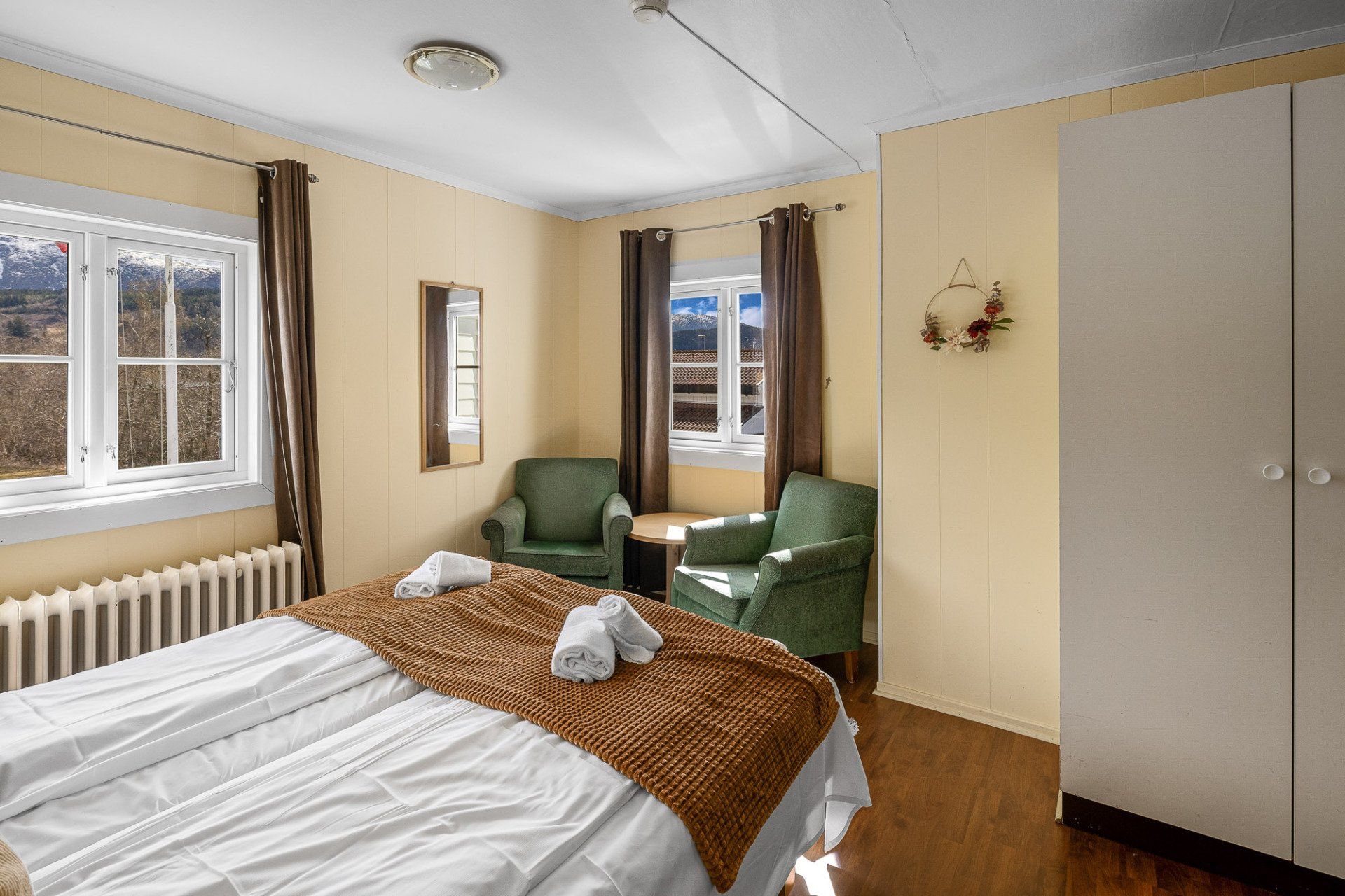 Neat bedroom with twin beds, green chairs, windows, and a white wardrobe