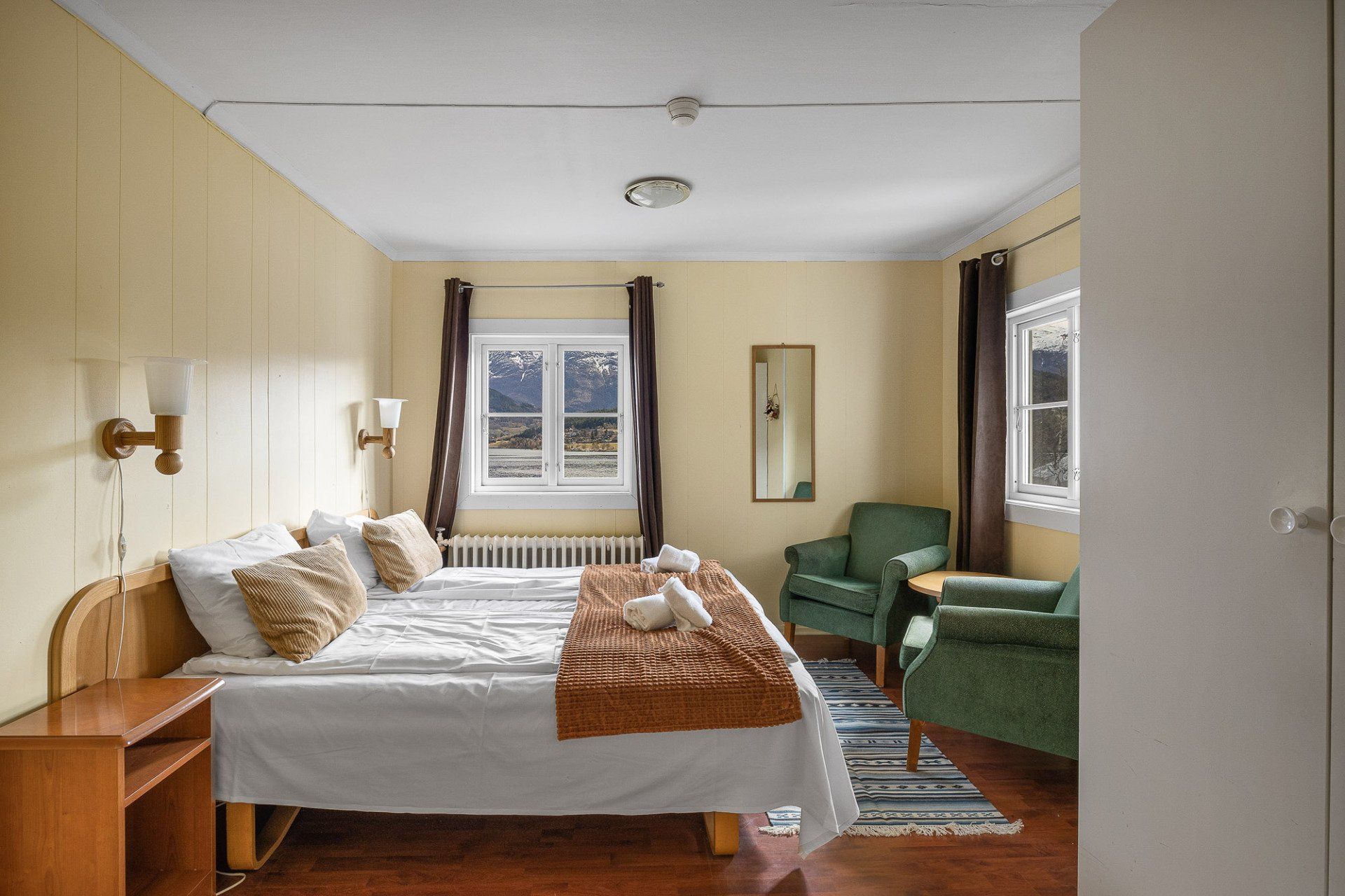 Cozy bedroom with a bed, green chairs, windows, and warm beige walls