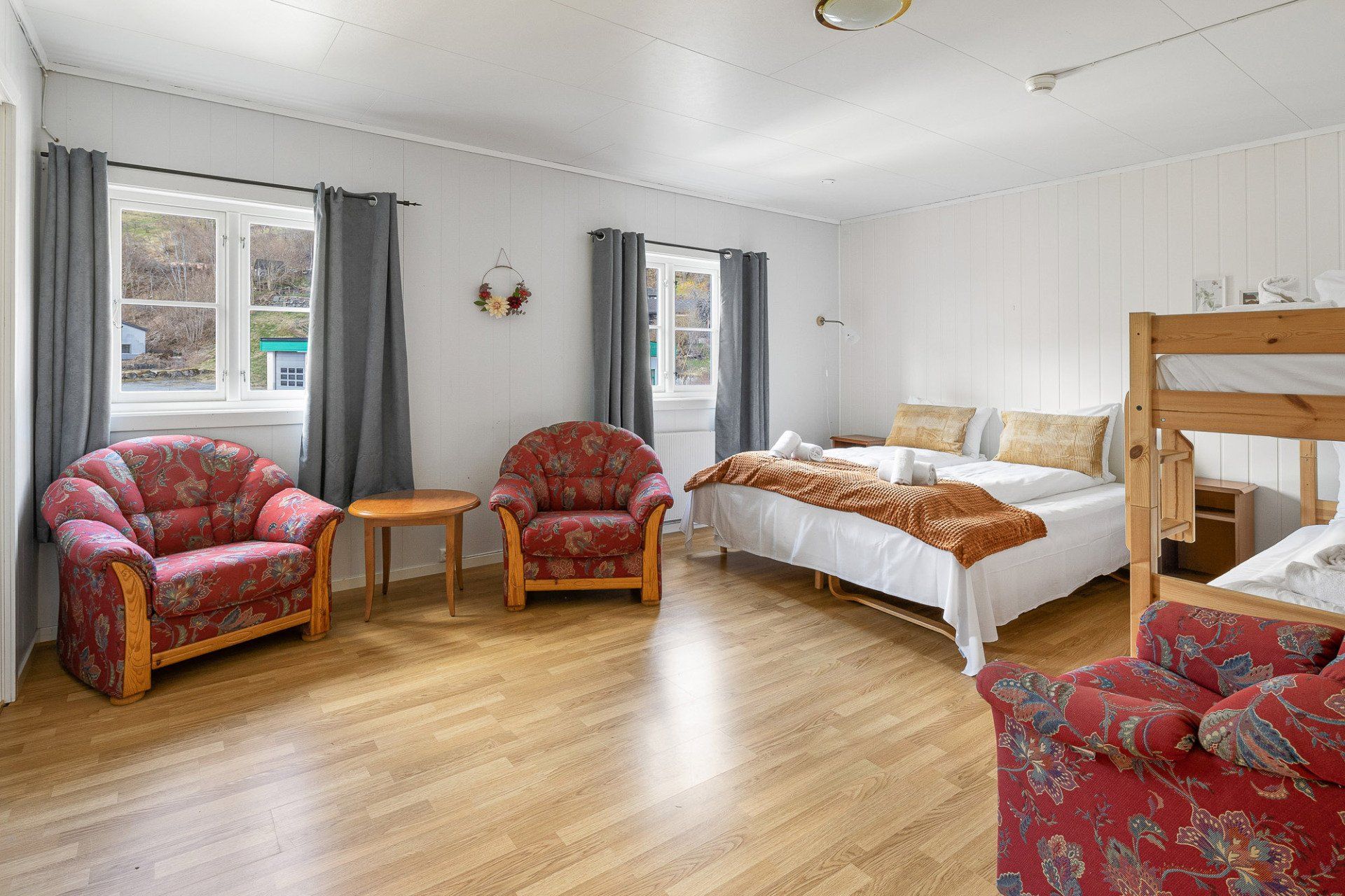 Bright bedroom with red armchairs, a bed, a bunk bed, and wood flooring by windows