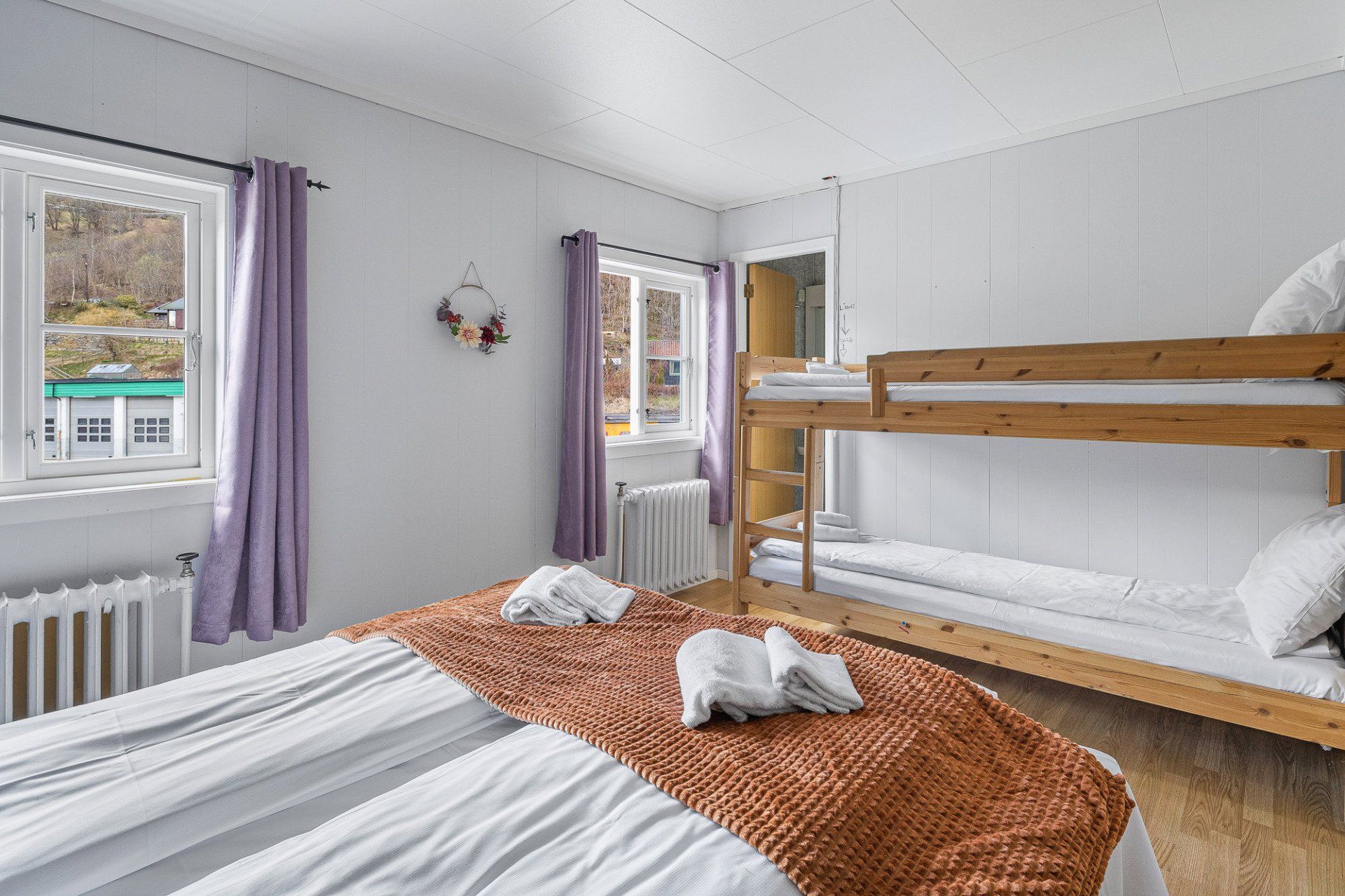 Bright bedroom with a bunk bed, white walls, purple curtains, and a small window seat.