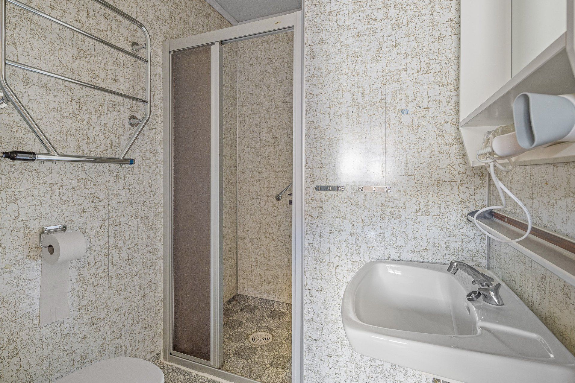 Small tiled bathroom with shower, sink, towel rack, and mirrored cabinet.