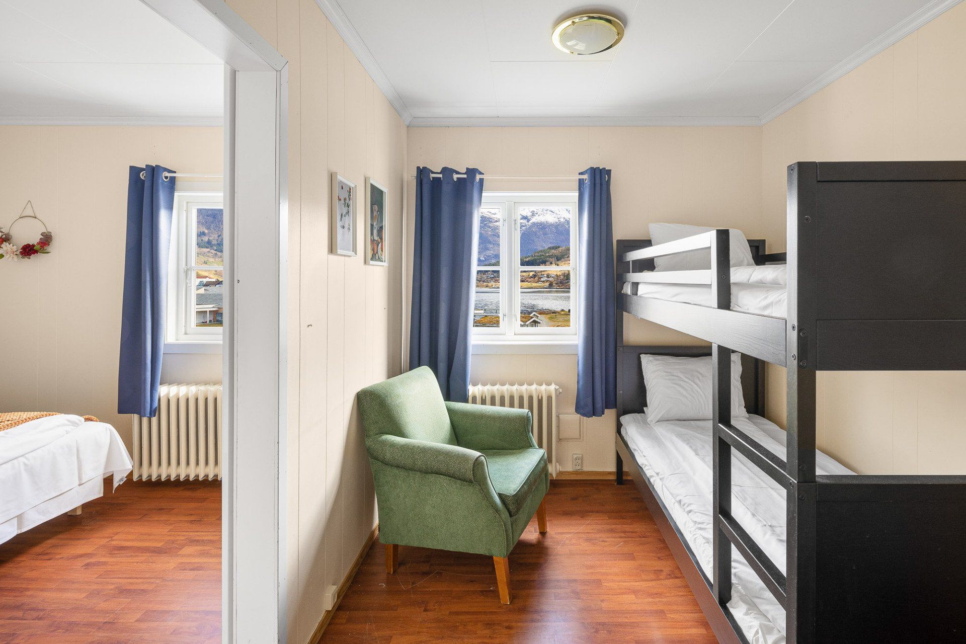 Small room with bunk beds, green armchair, and blue curtains by a window.