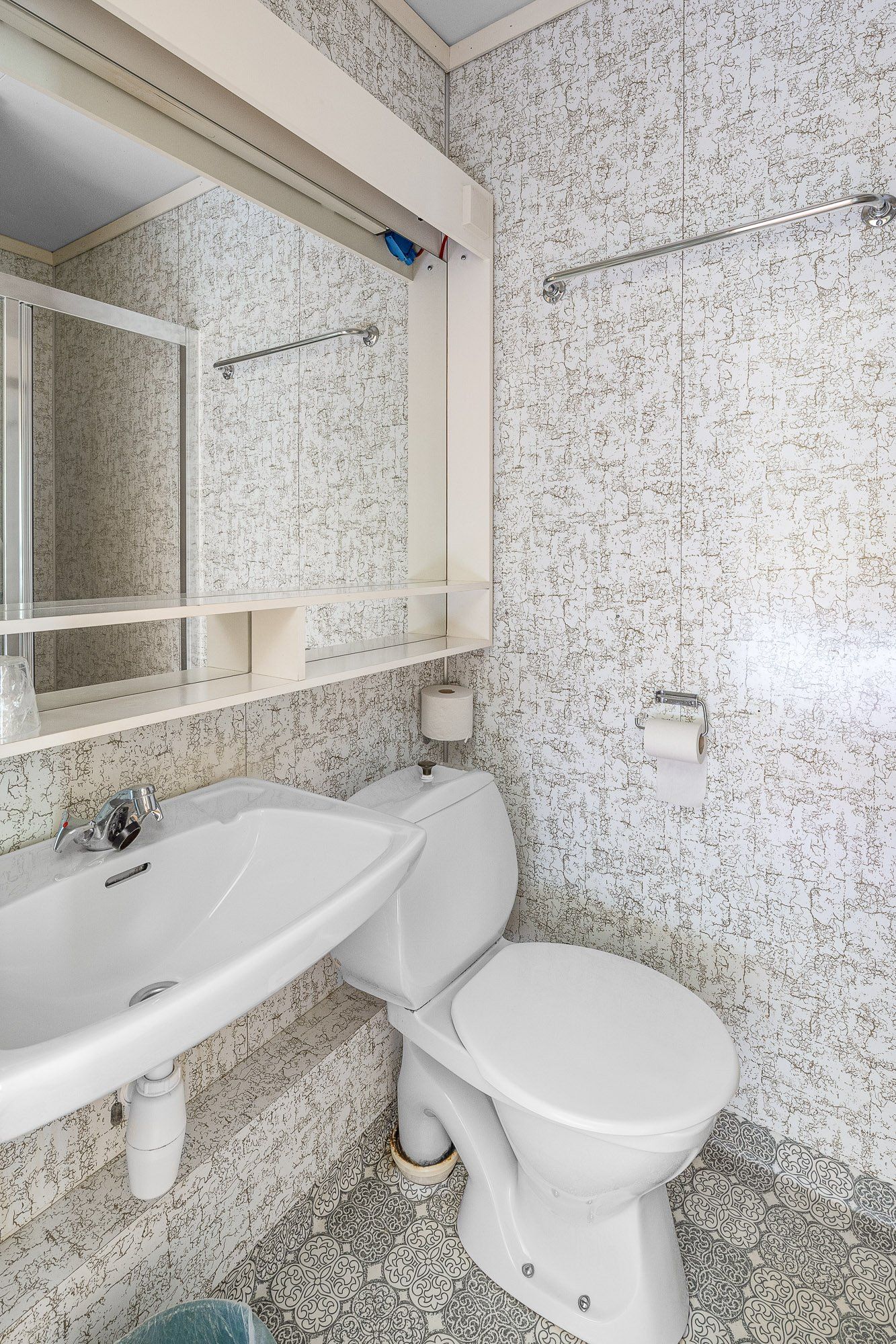 Small tiled bathroom with sink, toilet, mirror, and shower area