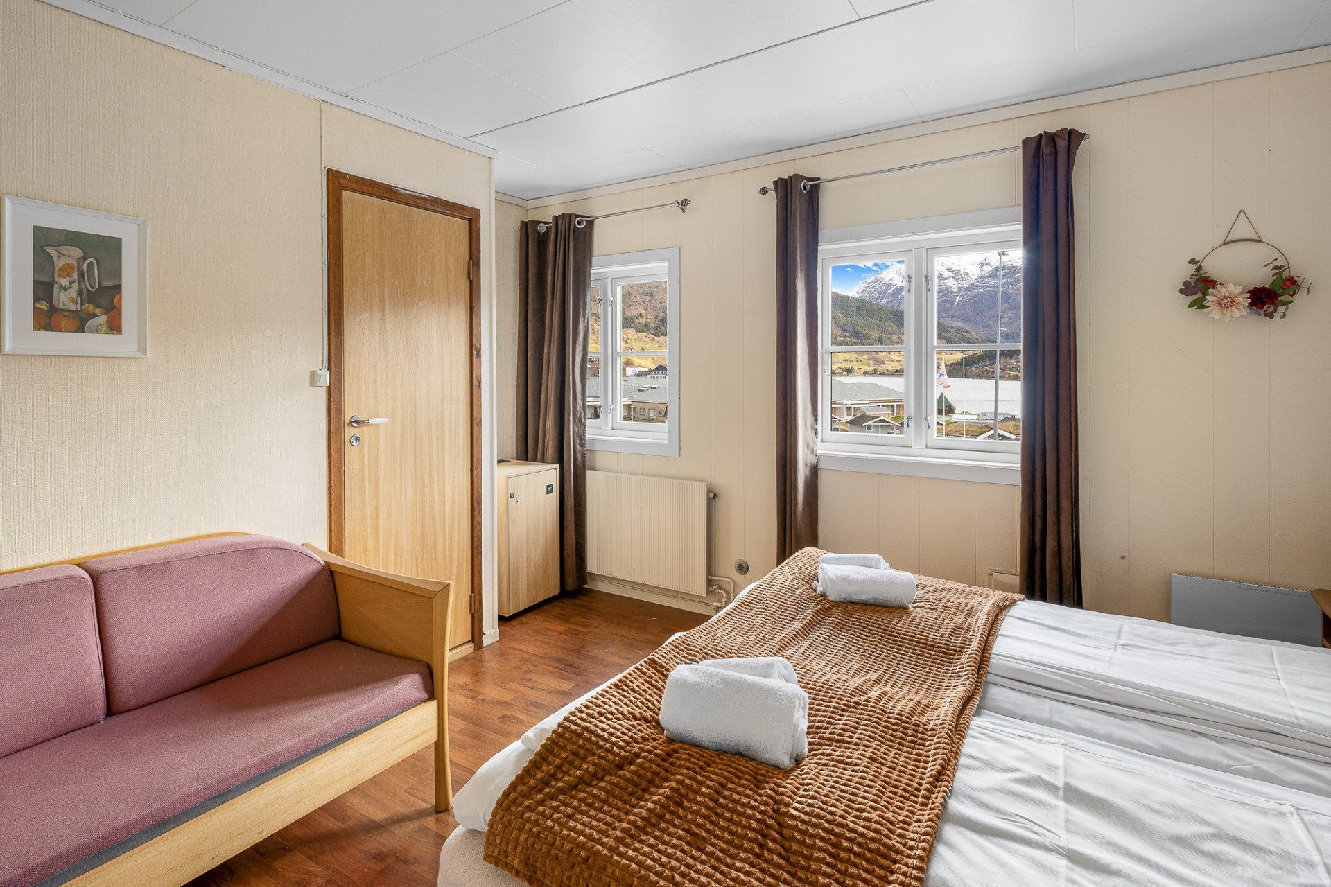 Cozy bedroom with pink sofa, twin beds, window view, and wooden door