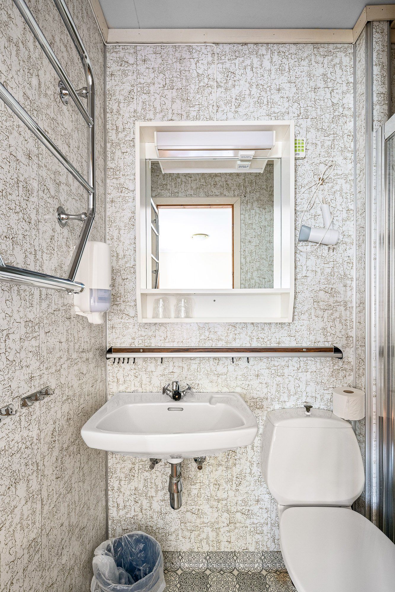 Small bathroom with sink, mirror, toilet, and floral wallpaper.